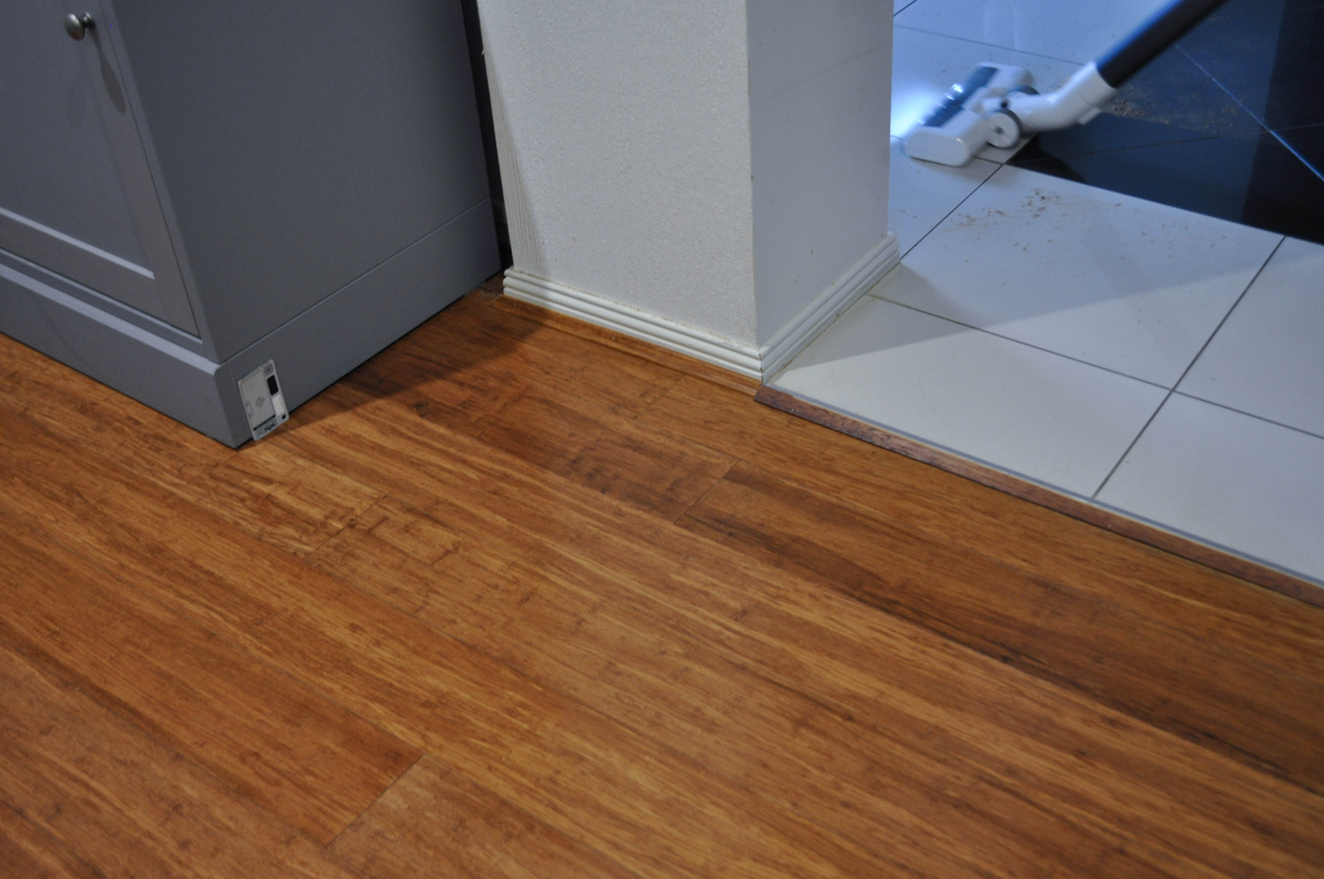 showing a room where the floor is covered with bamboo flooring abutting to white ceramic tiles. A grey cabinet is on top of the bamboo
	floor.