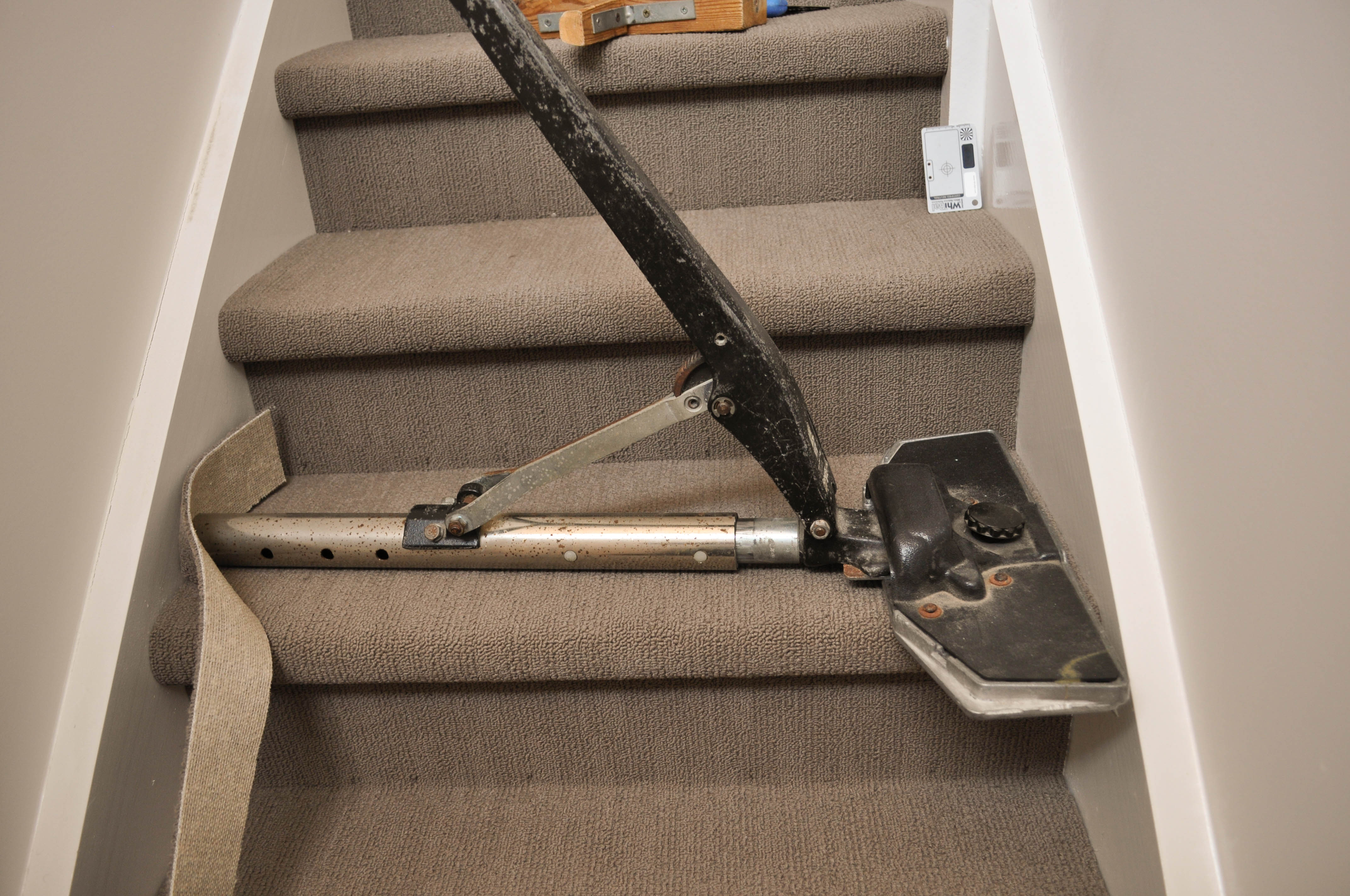 showing three steps with a power stretcher positioned across one and in action stretching the carpet across the step
to tense it and remove any ripples the carpet may have. Carpet is being laid by Concord Floorsin a house in Point Cook, Werribee, Vic 3030.
