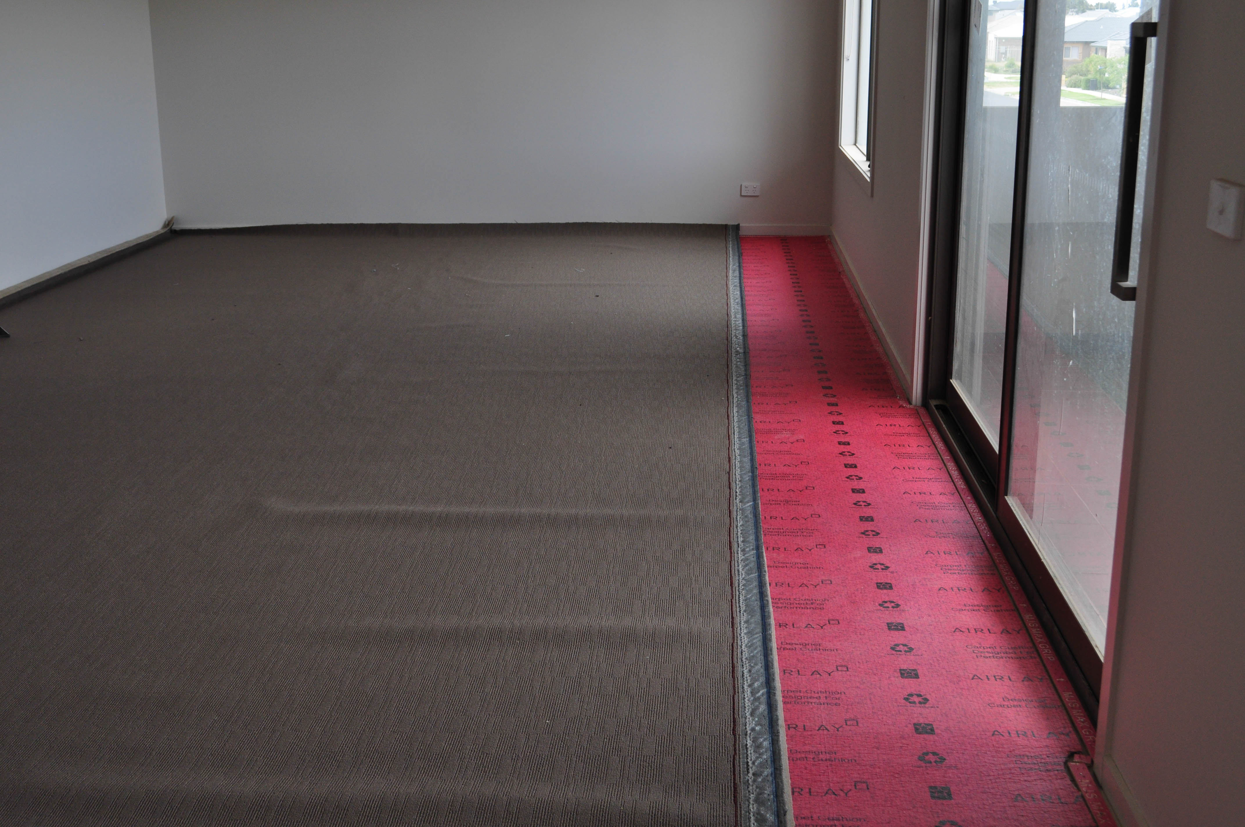 carpet laying process under way by Concord Floors in a home in Werribee, where pattern matching is required, showing a roll of carpet in a room, stretched out, on top of installed red underlay in a home in
 Point Cook, Werribee.
