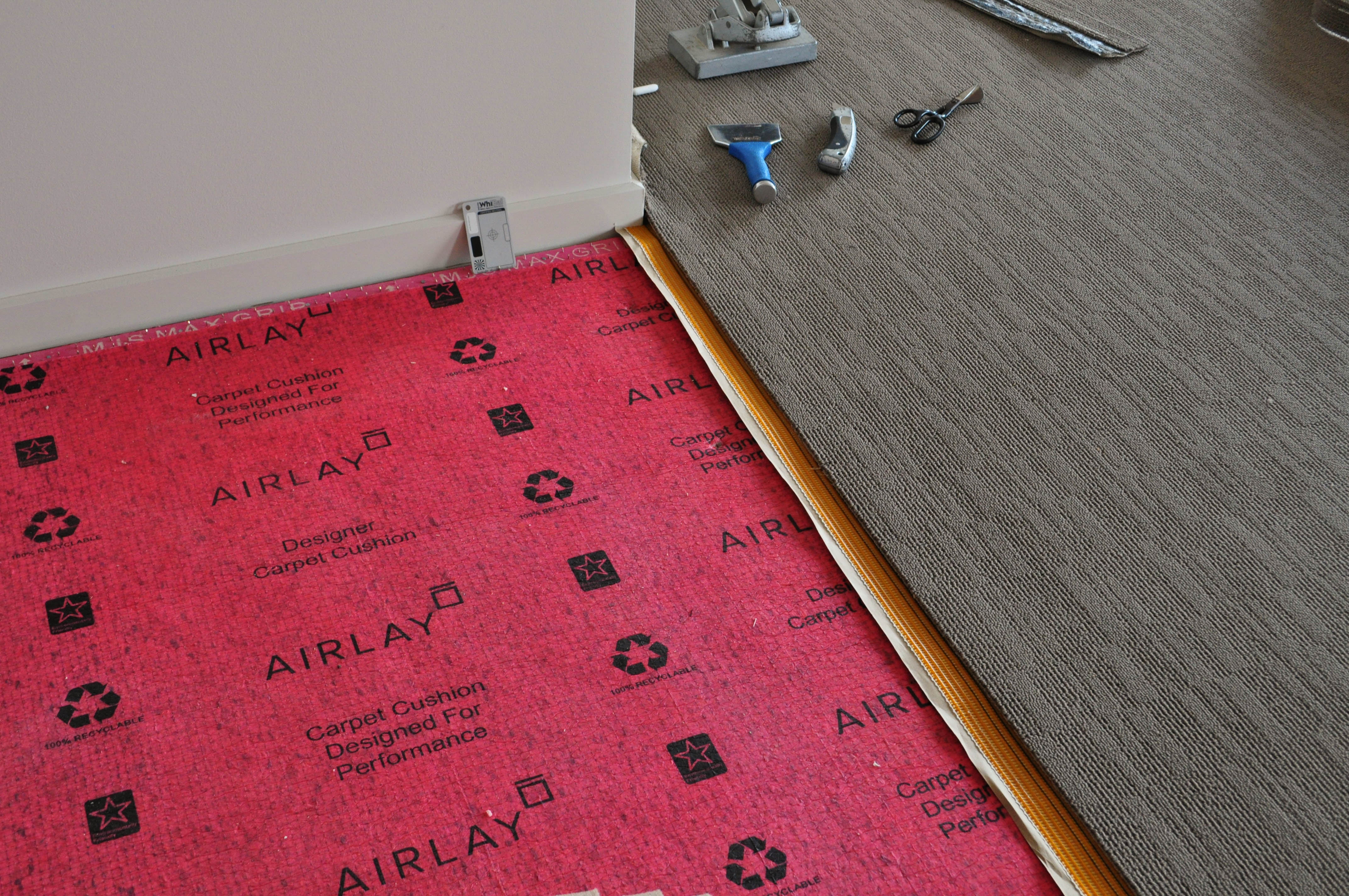 the interior of a modern home, with a grey wall, a modern beige colored, patterned carpet, and the red underlay still showing. The home is in Point Cook, 
 Werribee and the carpet was installed by Concord Floors. It is beautifull.
