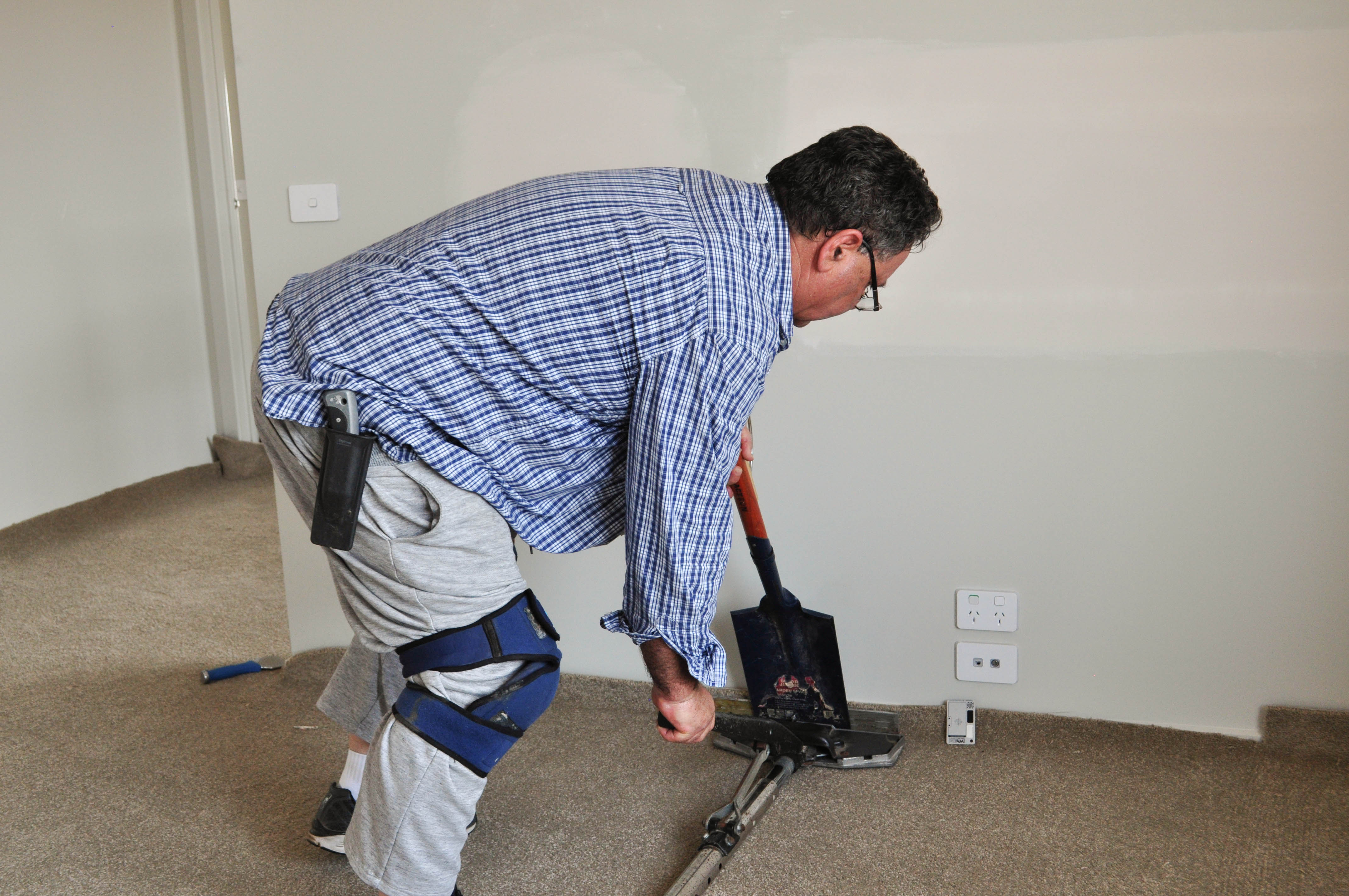 a slab of carpet with ripples in it, in a room that has been lifted of the gripper and where the telescopic head of the power stretcher
has been applied against the carpet gripping it and stretching it. The picture shows a carpet layer using the power stretcher to forcefully stretch the carpet and remove the
ripples.