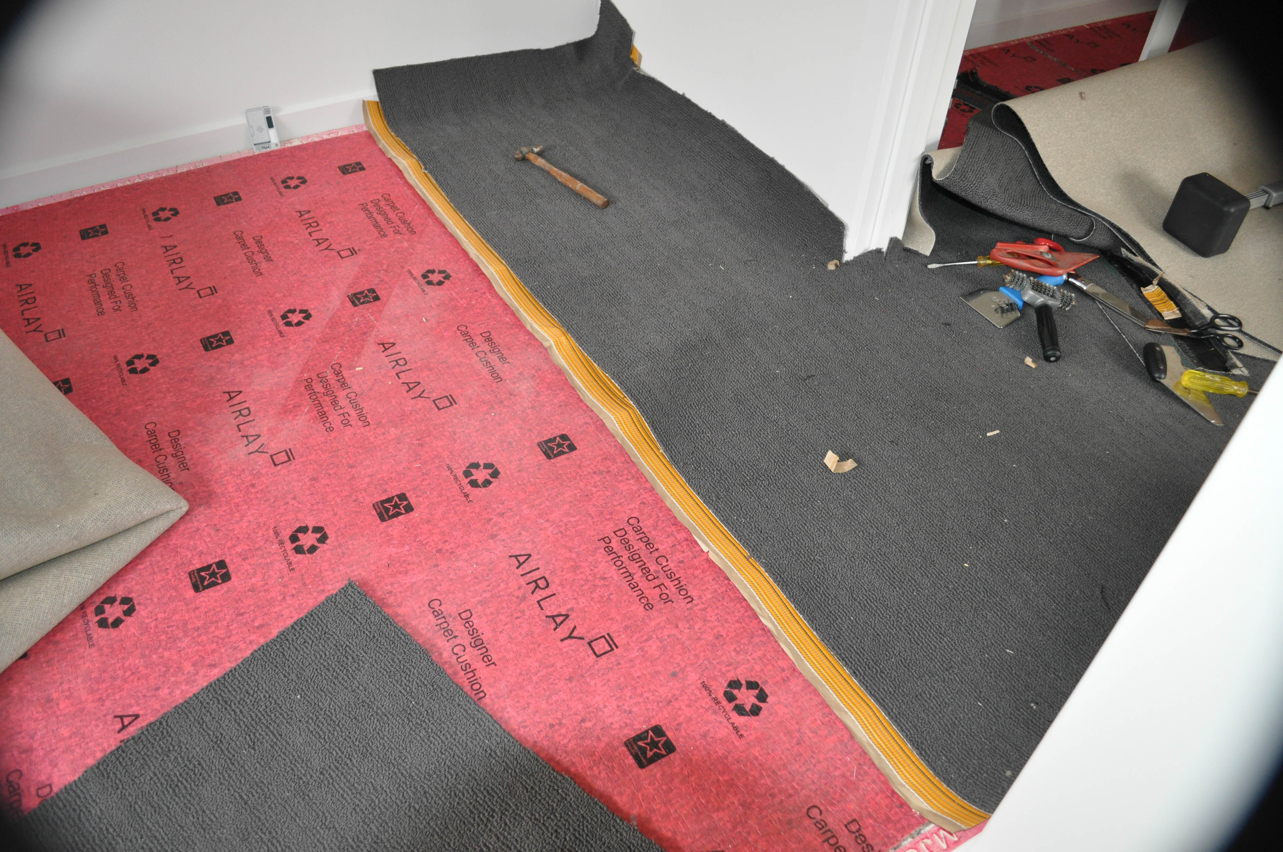 a body of carpet of charcoal color, positioned where it will remain after the join is executed, where the carpet edge has been prepared
                for a join with the adhesive tape underneath the carpet edge.