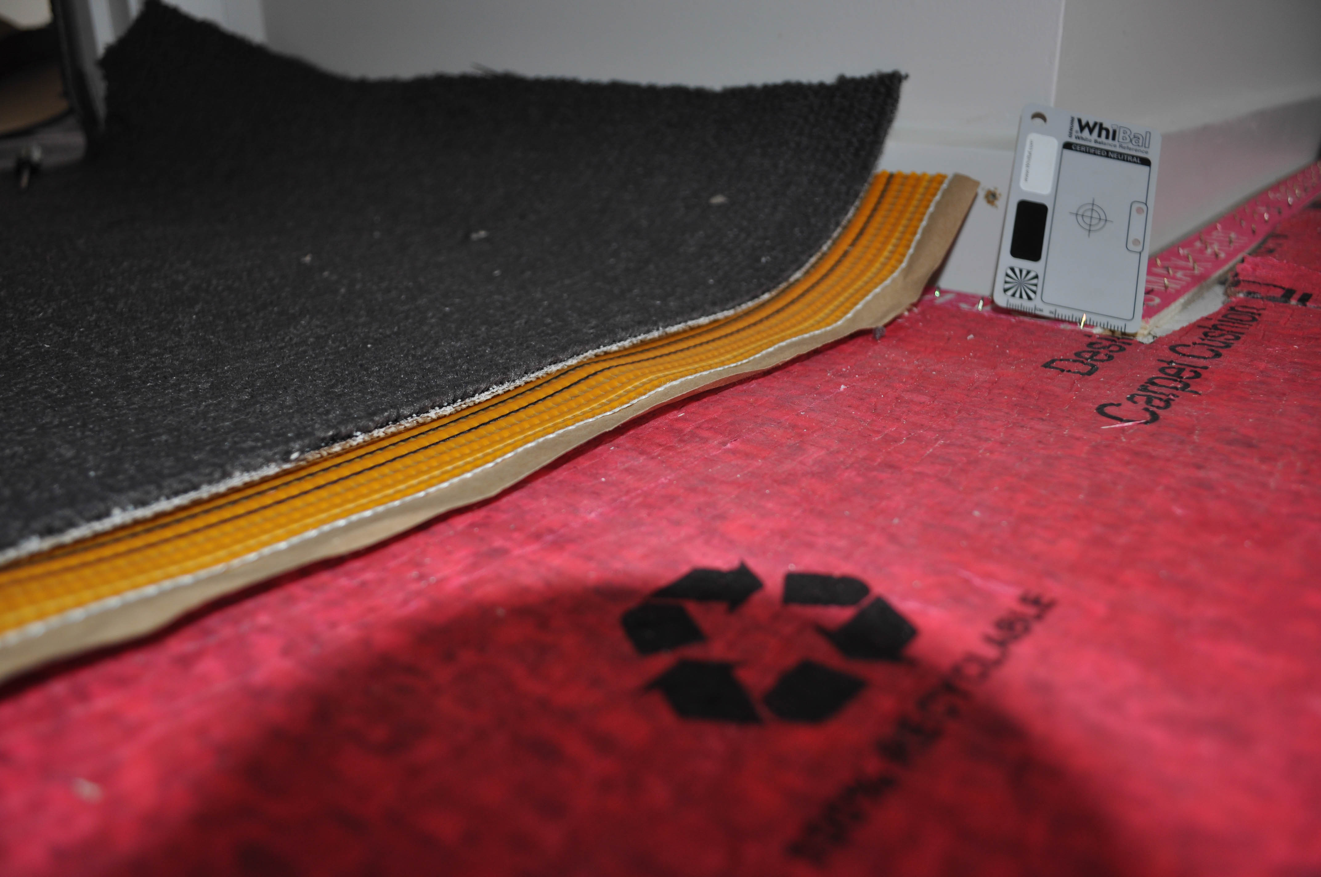 a body of charcoal colored carpet with the edge prepared for a join. The adhesive tape is half way underneath the carpet edge.