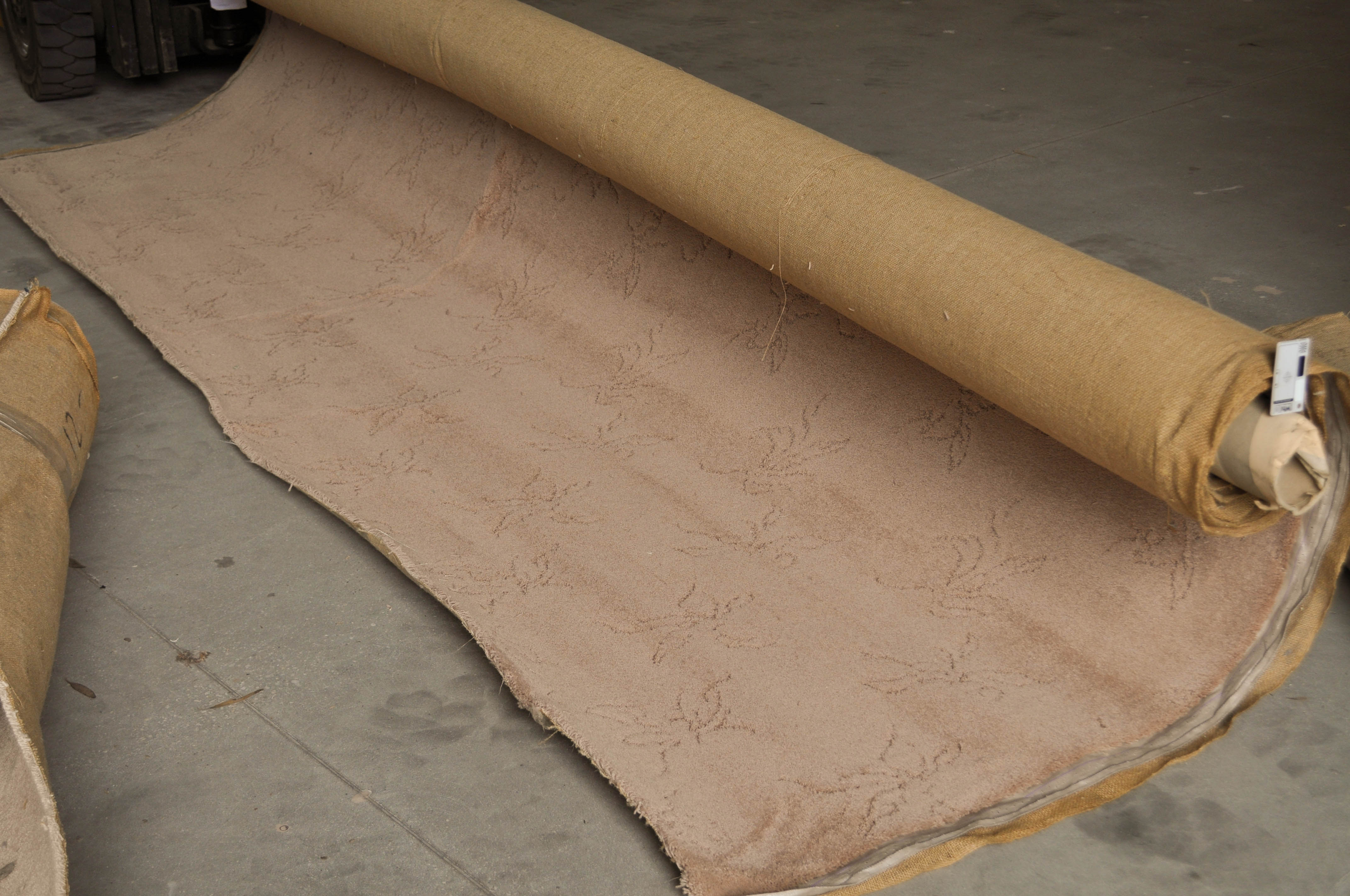 pink colored, patterned plush-pile carpet on the prong of a forklift being rolled out in the warehouse of Concord Floors.