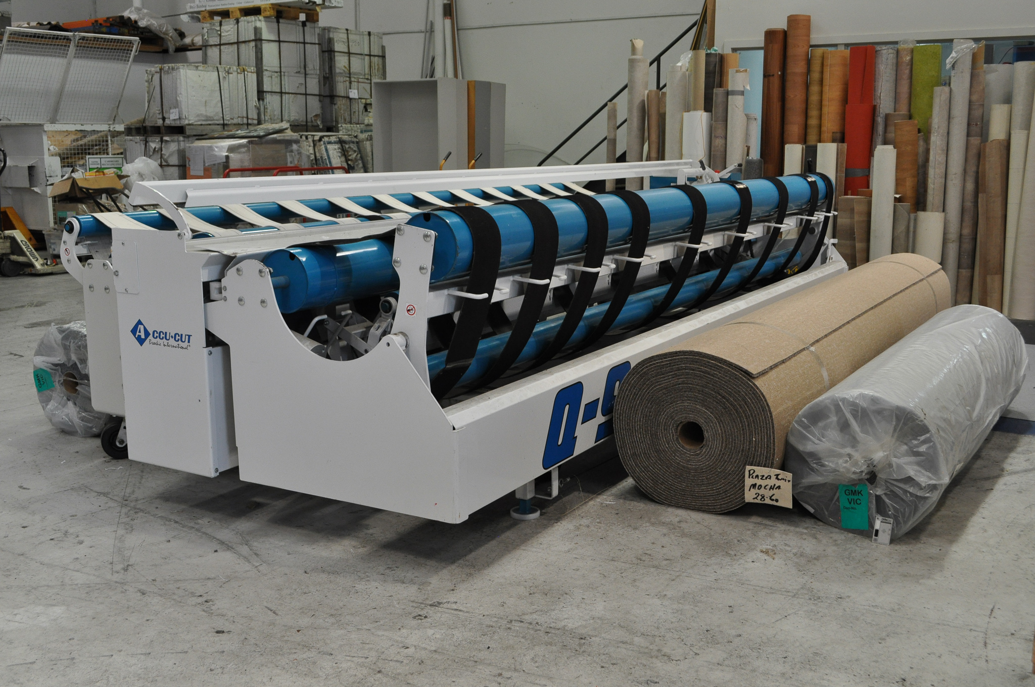 a carpet cutting machine with 2 rolls of carpet next to it ready to be cut, and installed by Concord floors, in a Concord floors warehouse.
