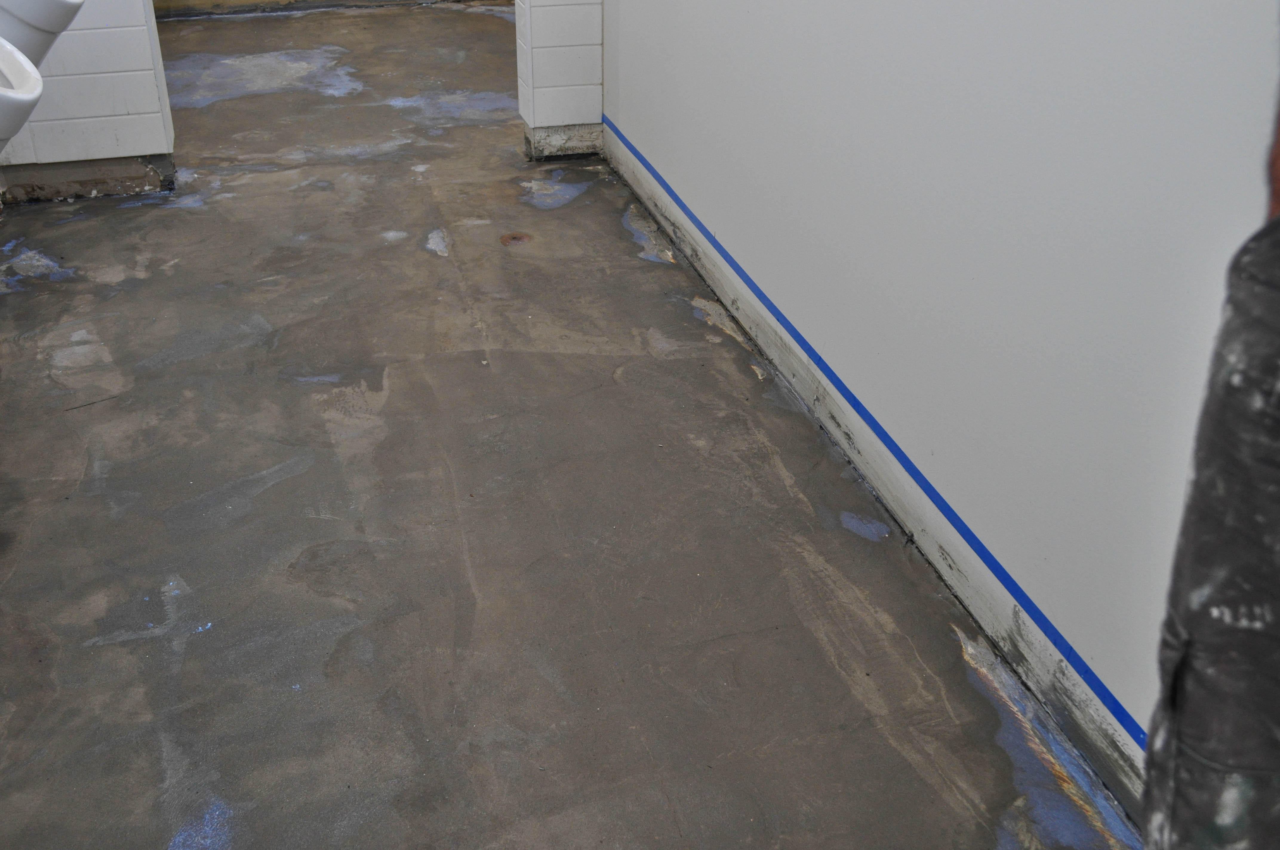 showing a room with a newly prepared toilet floor with floor leveller applied and primer liquid spread on it ready for the vinyl installation on top of it.