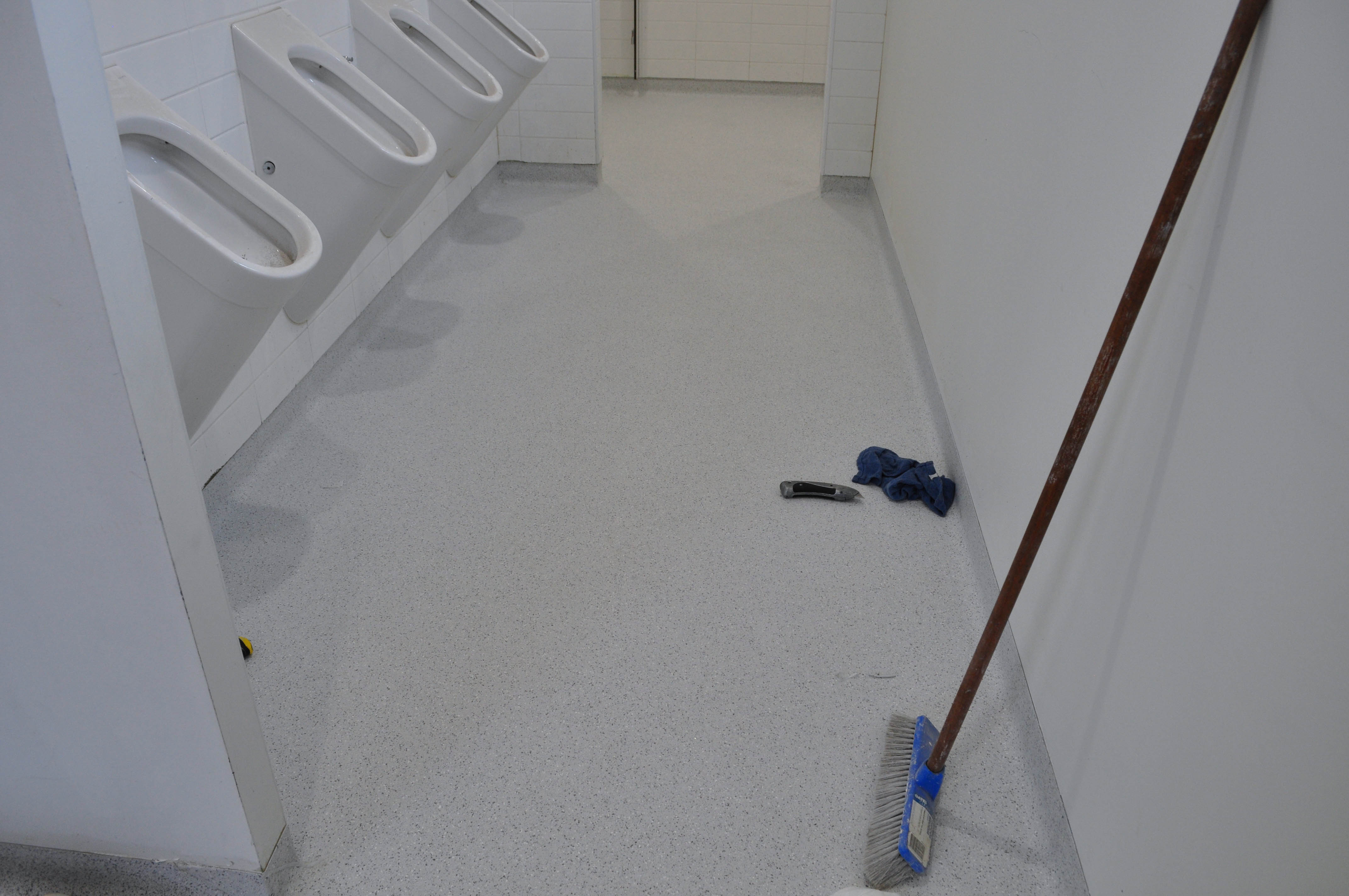 showing the floor of a of the entire toilet in which the floor has been covered by vinyl and the vinyl is coved up the wall and the whole job is finished.