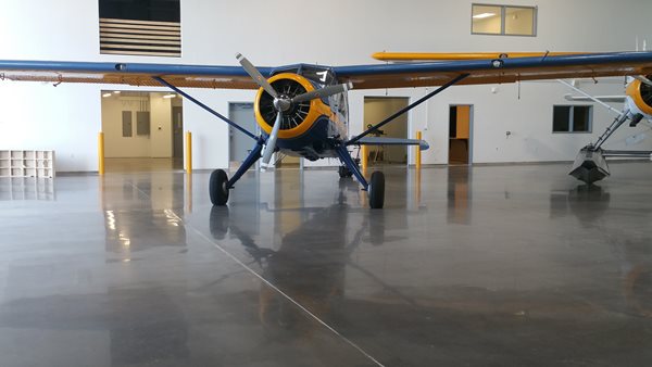 showing a large room with a newly polished concrete floor with an airoplane parked on it. The floor is an grey color.