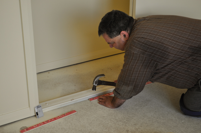 carpet layer affixing the carpet gripper to the floor in a room.