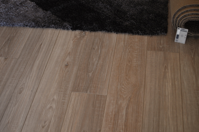 the picture shows 12mm thick oak laminate floorboard laid by Concord Floors in a room with a rug on top of it and the quiet 
  enjoyment the occupants of the house are having as a result of the laminate flooring's installation. The home is in the suburb of Hoppers Crossing Vic 3029.
