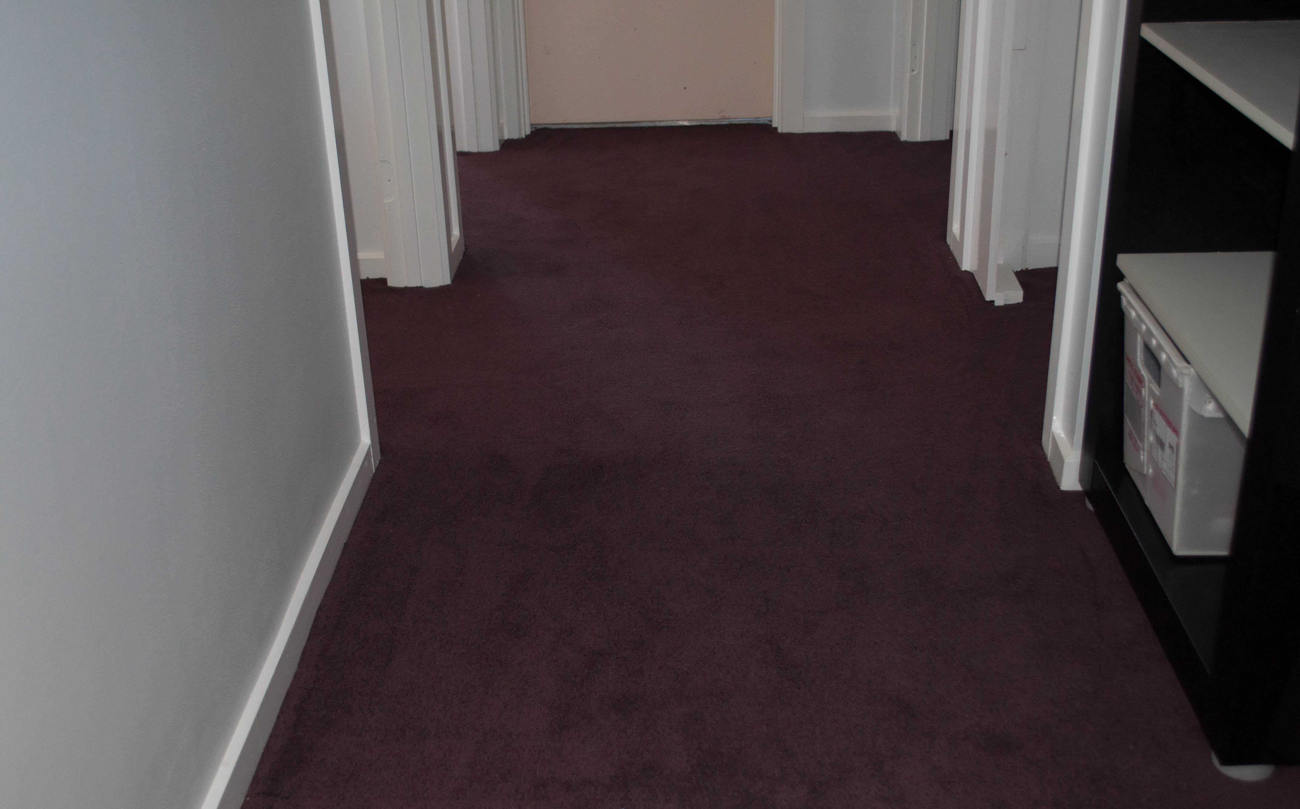 The carpet laying process is completed here. The carpet is a plain twist pile wool carpet of aubergine color and the wall of this wide------
 passage is a lavender grey color.The home is in the suburb of Melton Vic 3337 and the laying of the carpet is being done by Concord Floors.