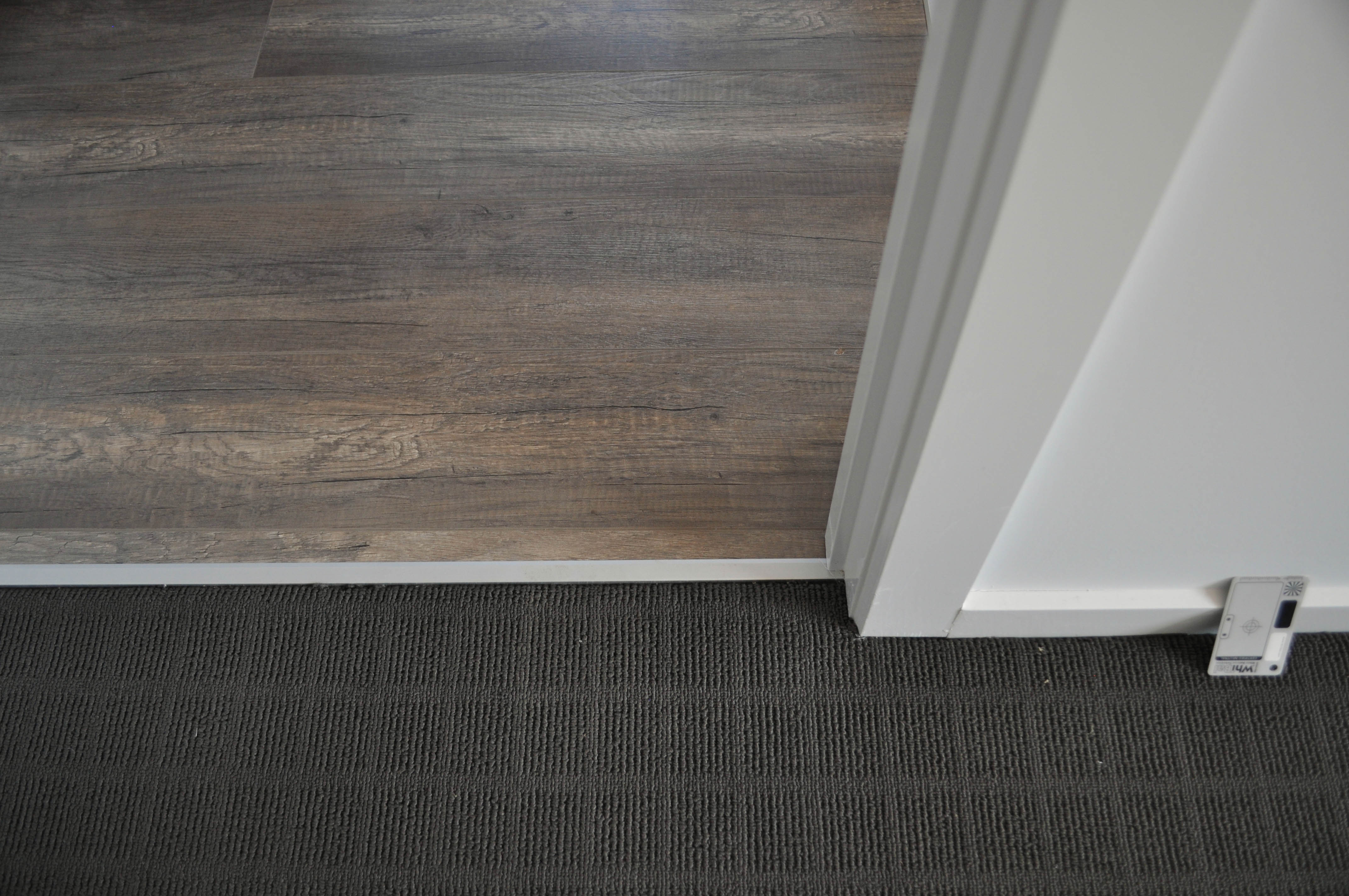 showing 12mm thick weathered oak laminate flooring installed in a room in the suburb of Werribee Vic 3340 by 
              Concord Floors next to patterned polypropelene, dak grey carpet and painted walls showing the interplay of the materials and their colors to produce
              harmony in the color scheme of interior decor in this home.It also shows the hard top surface of the laminate flooring which is even and the picture illustrates the ease 
              with which the surface of a laminate floor can be cleaned. The home is in the suburb of Hoppers Crossing, Vic 3029 and the laminate floorboards and the 
              carpet was supplied and laid by Concord Floors.