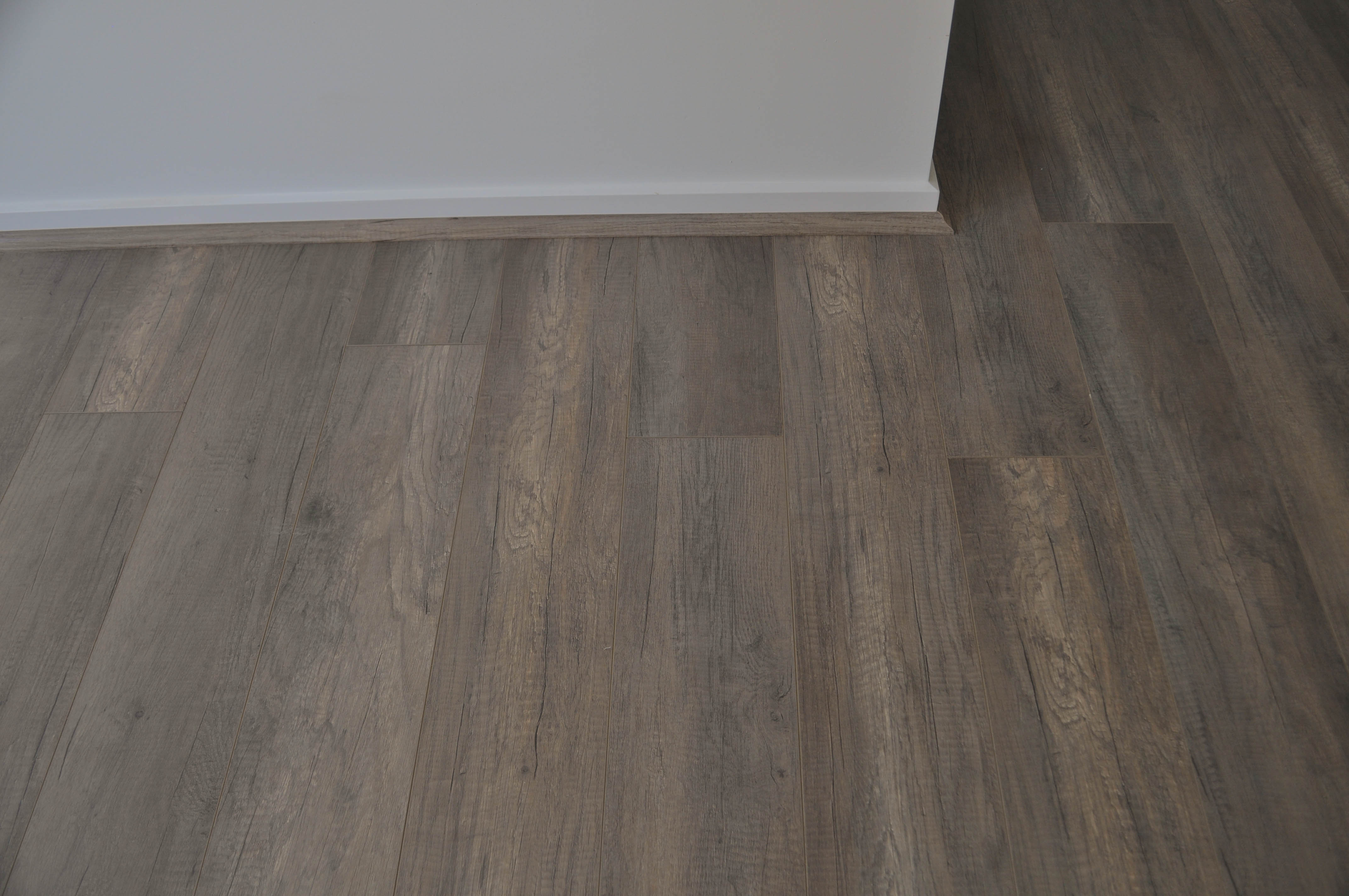 showing 12mm thick grey oak laminate flooring installed in a room in the suburb of Werribee Vic 3340 by 
  Concord Floors next to patterned polypropelene, dak grey carpet and painted walls showing the interplay of the materials and their colors to produce
harmony in the color scheme of interior decor in this home.It also shows the hard top surface of the laminate flooring which is even and the picture illustrates the ease 
with which the surface of a laminate floor can be cleaned. The home is in the suburb of Hoppers Crossing, Vic 3029 and the laminate floorboards and the 
carpet was supplied and laid by Concord Floors.