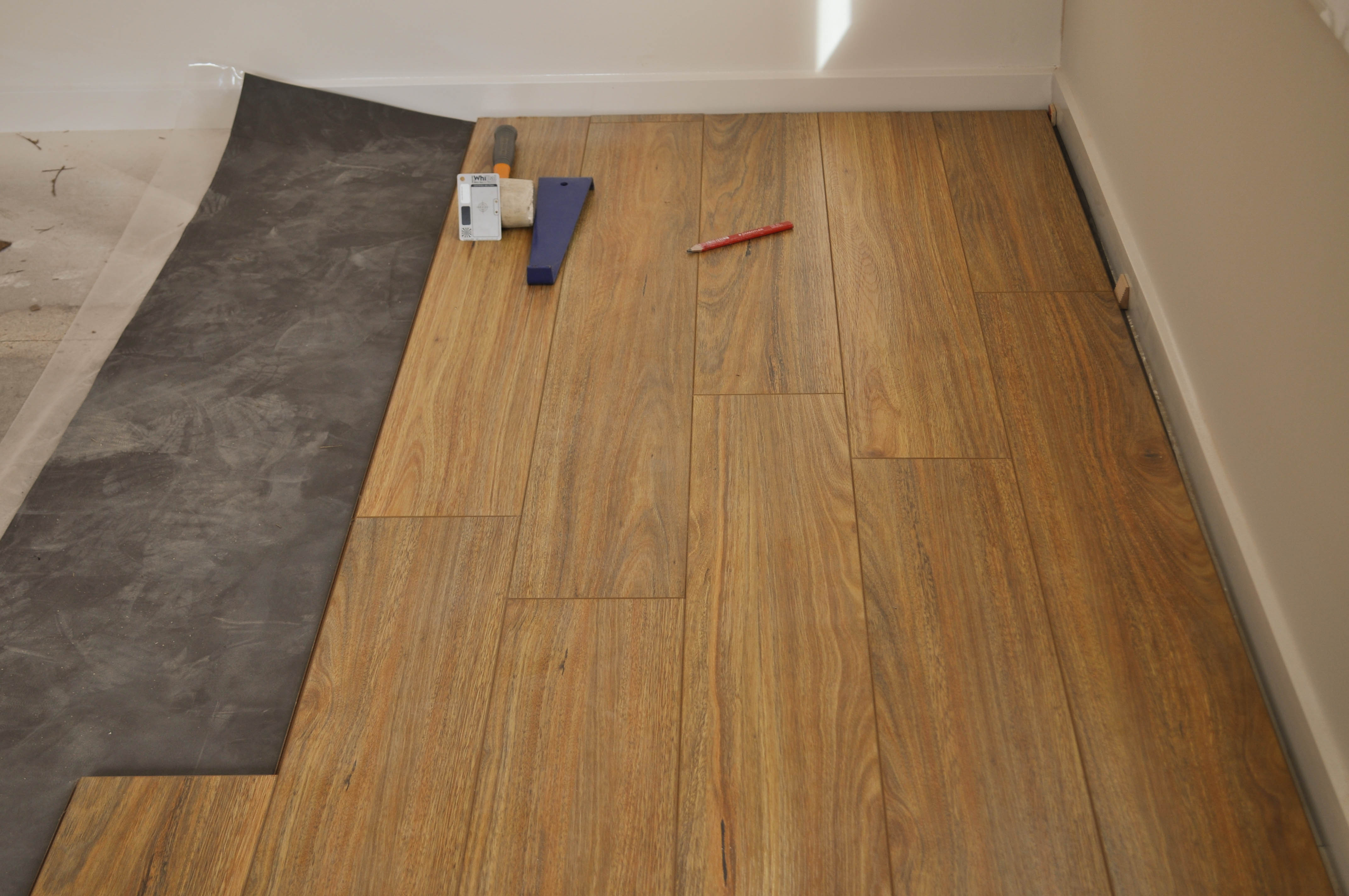 this picture shows a room in which 5 rows by the entire length of the room of 12mm thick laminate floorboards, in this
 case 12mm thick Spotted Gum, have been laid over black accoustic underlay. The particle board sub-floor has been prepared to receive the underlay and the underlay rolled out 
 to receive the floor boards. The row of floor boards next to the wall has 10mm thick wedges placed there so that the floorboards are kept 10 mm from the wall thus creating 
 a permanent expansion gap. The second row is installed by interlocking it into the first row and the third row into the second and the fouth into the third and the fifth 
 into the fourth. When the last board in the row that reaches the wall, reaches the wall, it is marked to the size to fit between the wall and the second last board and cut on that 
 mark. The excess balance of the board is then taken to the other side of the room to commence the next row. The tapping tool and the mallet is sitting on the flooring. This is 
 the process of installing/laying a floating floor. The room is in a home in the suburb of Point Cook, Werribee Vic 3030 and the boards were supplied and installed by
 Concord Floors. This is information as to how to install laminate flooring for the do it yourself floor board laminate flooring installer.