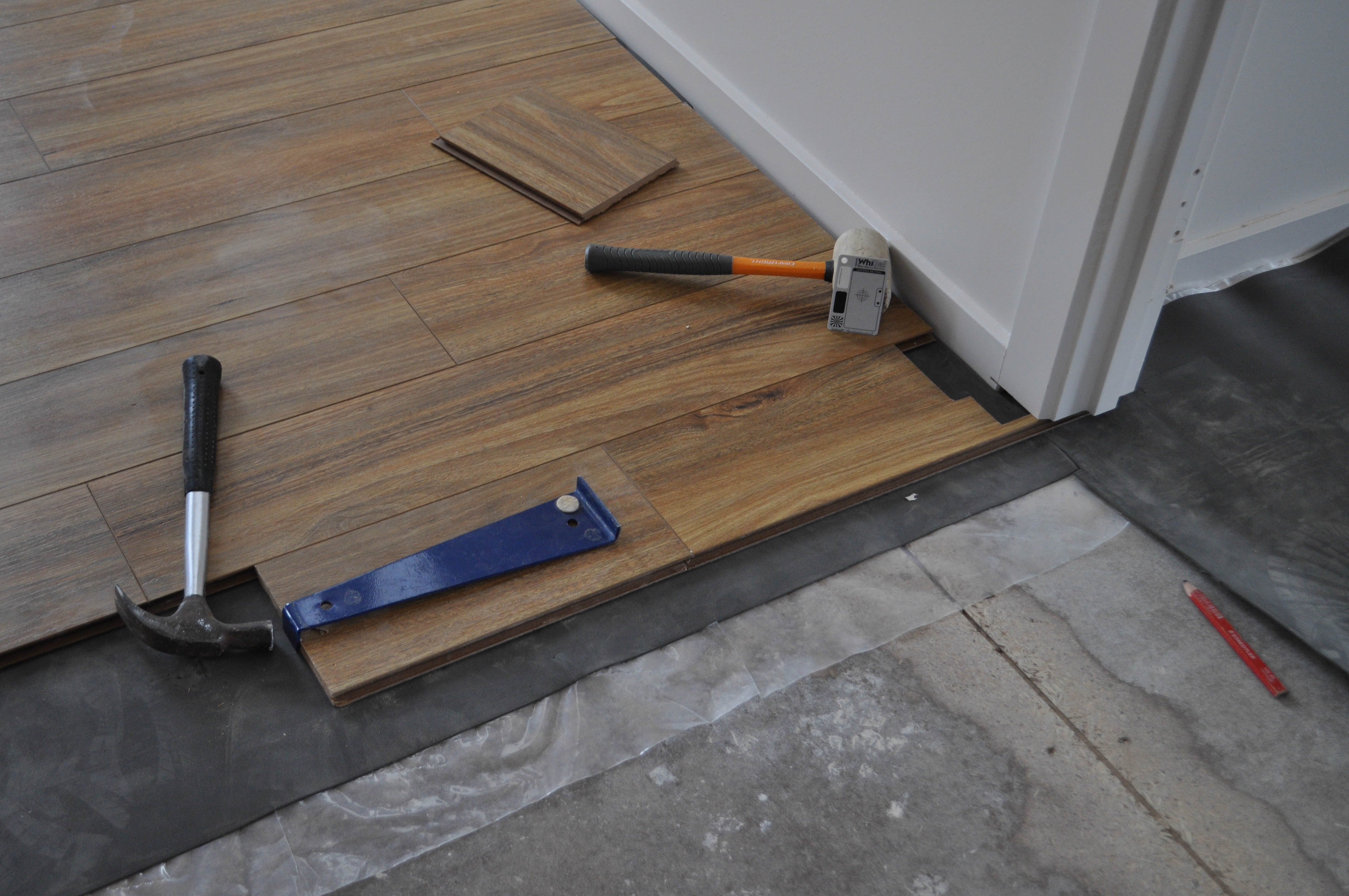 shows a door jamb, in a room, that has being undercut by an undercutting saw to create a cavity which will receive the laminate floorboard.
 The floorboard has been notched to fit smuggly inside this cavity so that the required expansion gap between the perimeter of the floorboard and the timber framework of the wall
 will be covered by the doorway architrave. The notched floorboard has been positioned, next to and facing the door jamb cavity, ready to be tapped iside the door jamb cavity. The picture
shows 12mm thick spotted gum laminated flooring being installed between two rooms in a house in the suburb of Point Cook, Werribee Vic 3030. On the floor boards is the tapping tool
with the boards are tapped into position and place and the hammer used for tapping. This is information as to how to install laminate flooring for the do it yourself floor 
board laminate flooring installer.