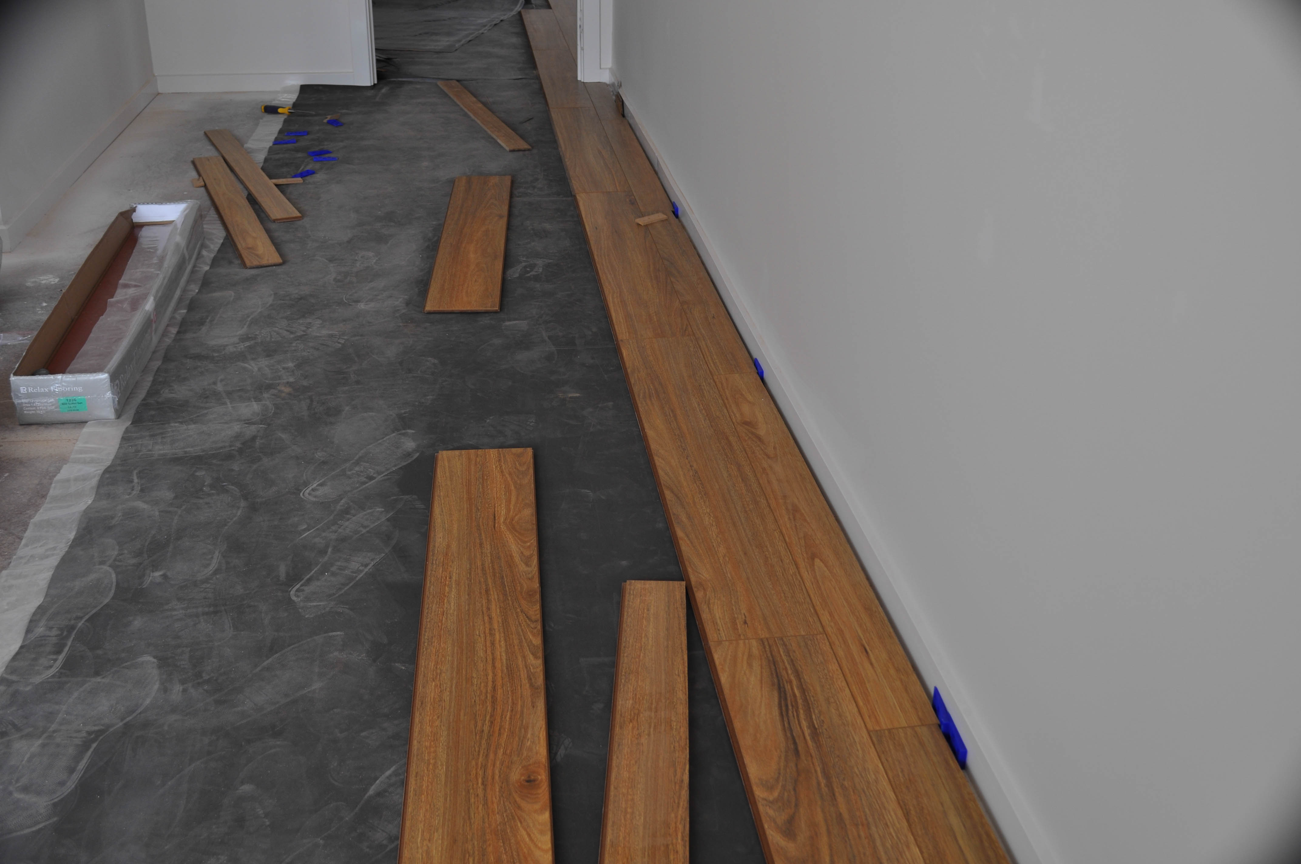 showing the first stage of the commencement of laying a laminate floor. The first row of laminate flooring is being laid on top 
of laid out underlay. It shows the ease with which the underlay is laid and the ease with which the laminate boards are placed into position and affixed to each other. 
Because of the ease of placing the boards together the picture also shows the quick speed with which a floor can be laid which reduces the cost of laying or installation.
So in an indirect way the picture shows the competitiveness of laminate flooring with the traditional hard flooring materials. The boards are 12mm thick spotted gum laminate
 flooring being installed in a room by Concord Floors in a home in the suburb of Werribee Vic 3340.