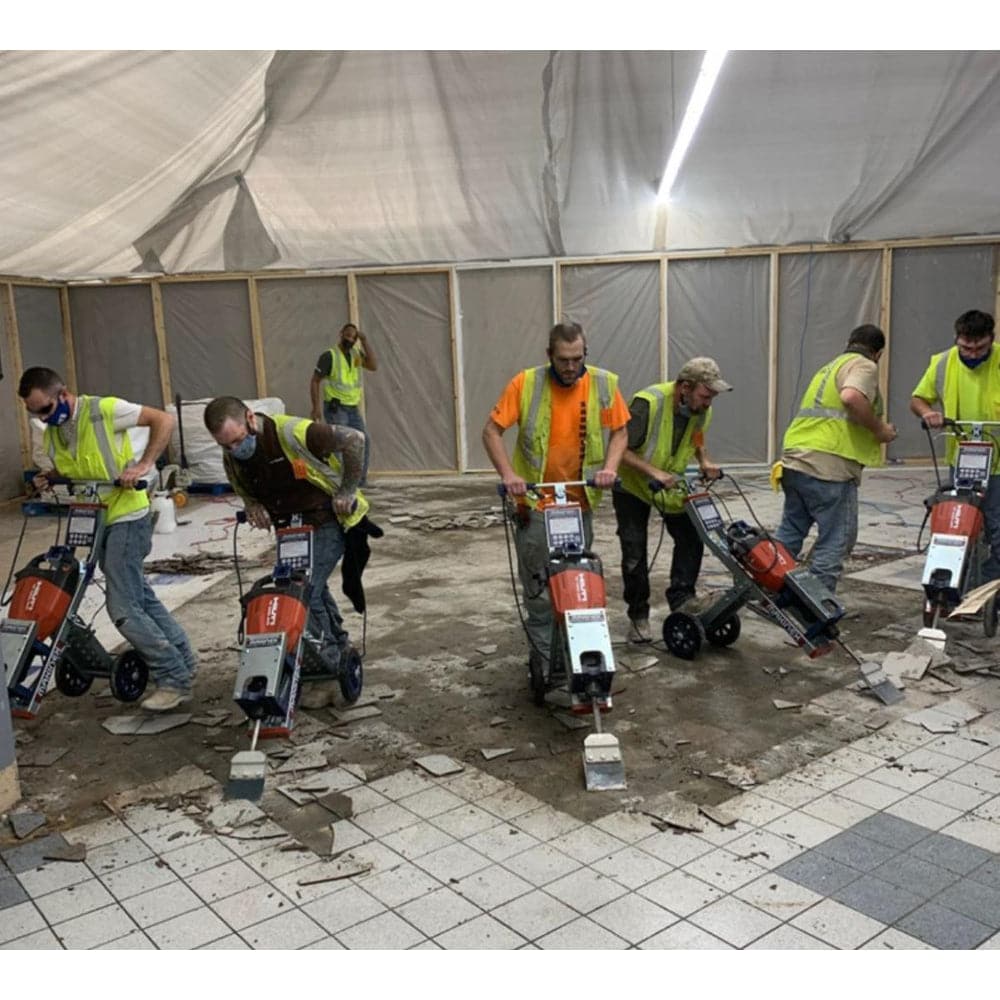 showing a large room with seven men with jackhammers pulling up existing ceramic tiles.