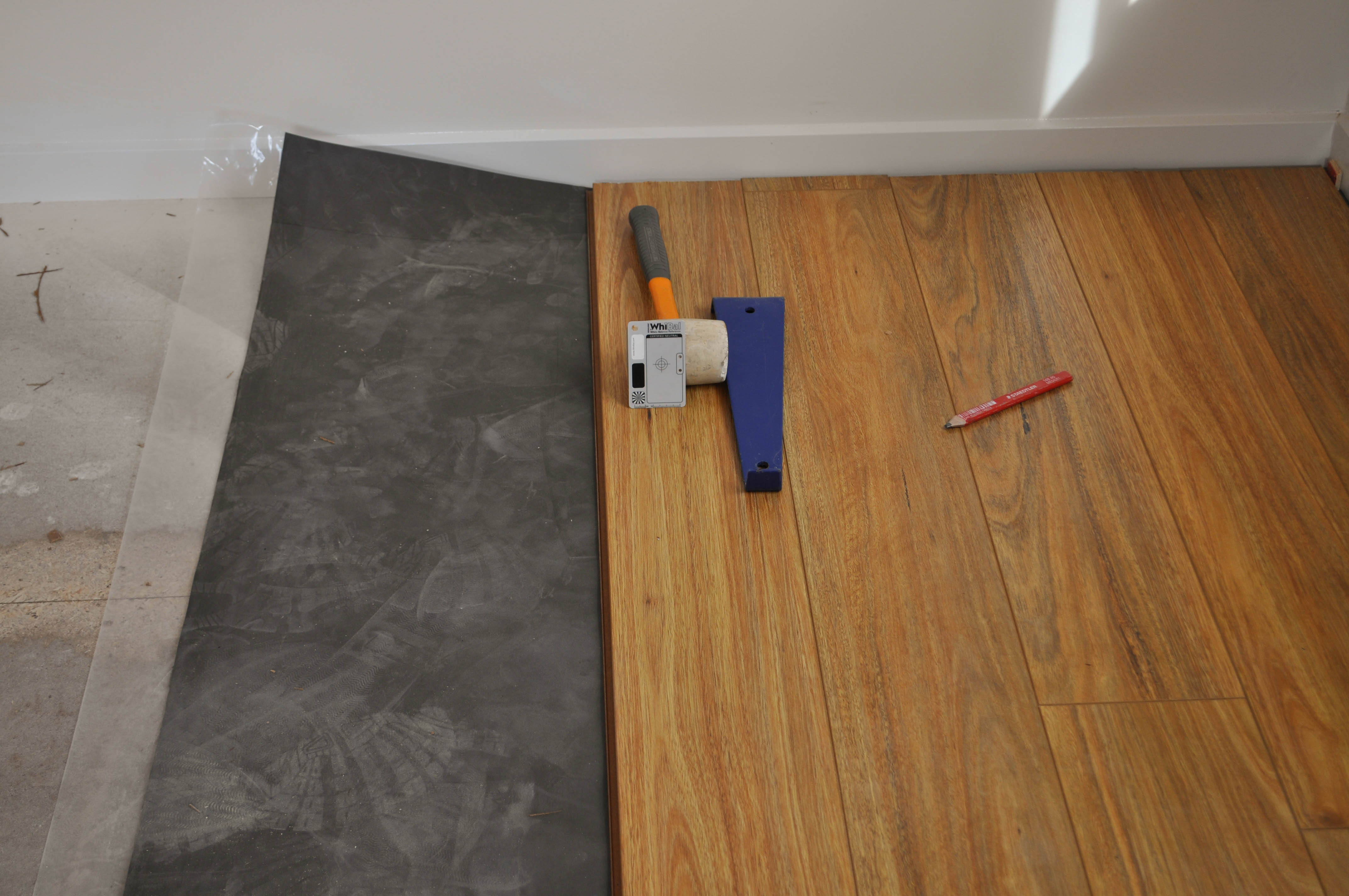 showing a room with laminate flooring installation process under way by Concord Floors, showing black underlay and a patch of installed laminate boards, orange coloured, 
 in a home in Point Cook, Werribee.